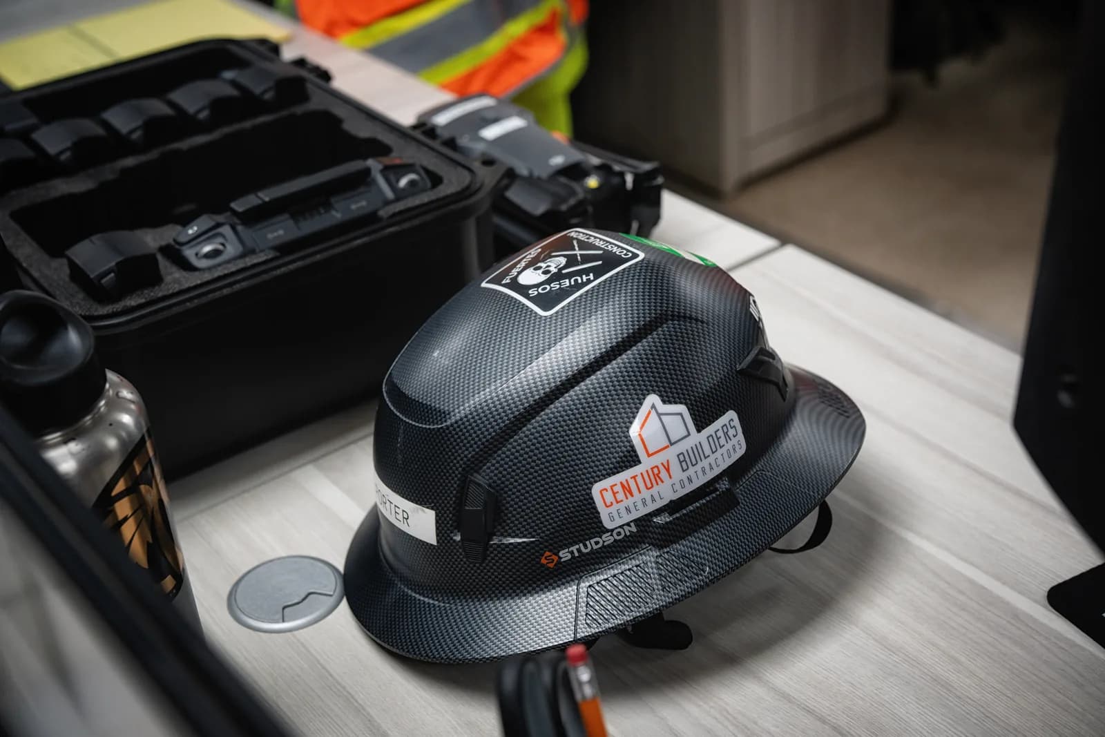 Century Builders branded carbon-fiber hard hat on a field-office desk